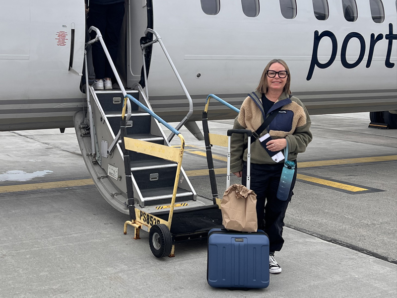 The Minimizer representative standing with luggage beside an airplane, ready to support a home transition.